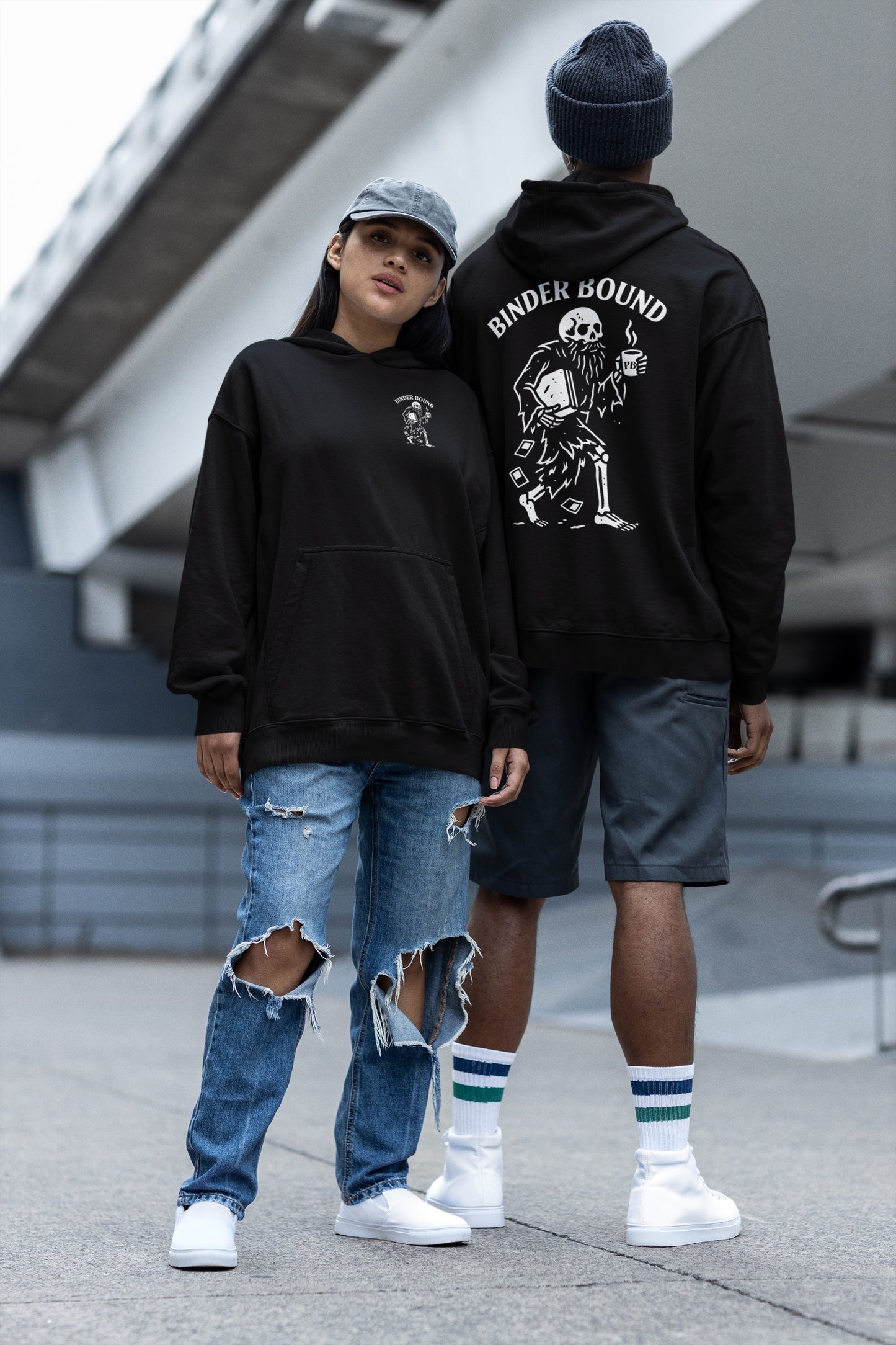 Two people wearing black hoodies with visible branding, standing outdoors.